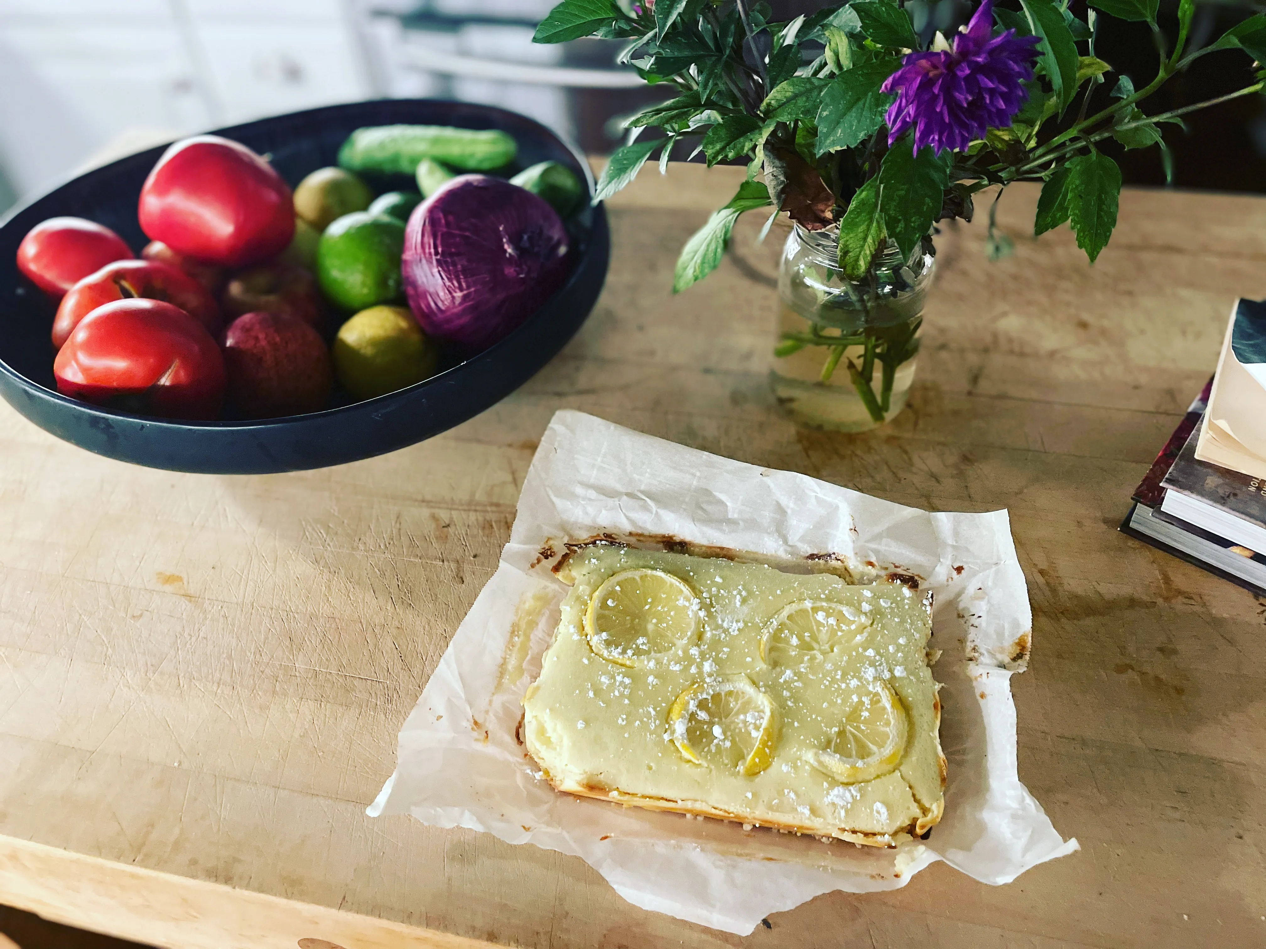 Lemon tart on parchment beside seasonal produce and flowers