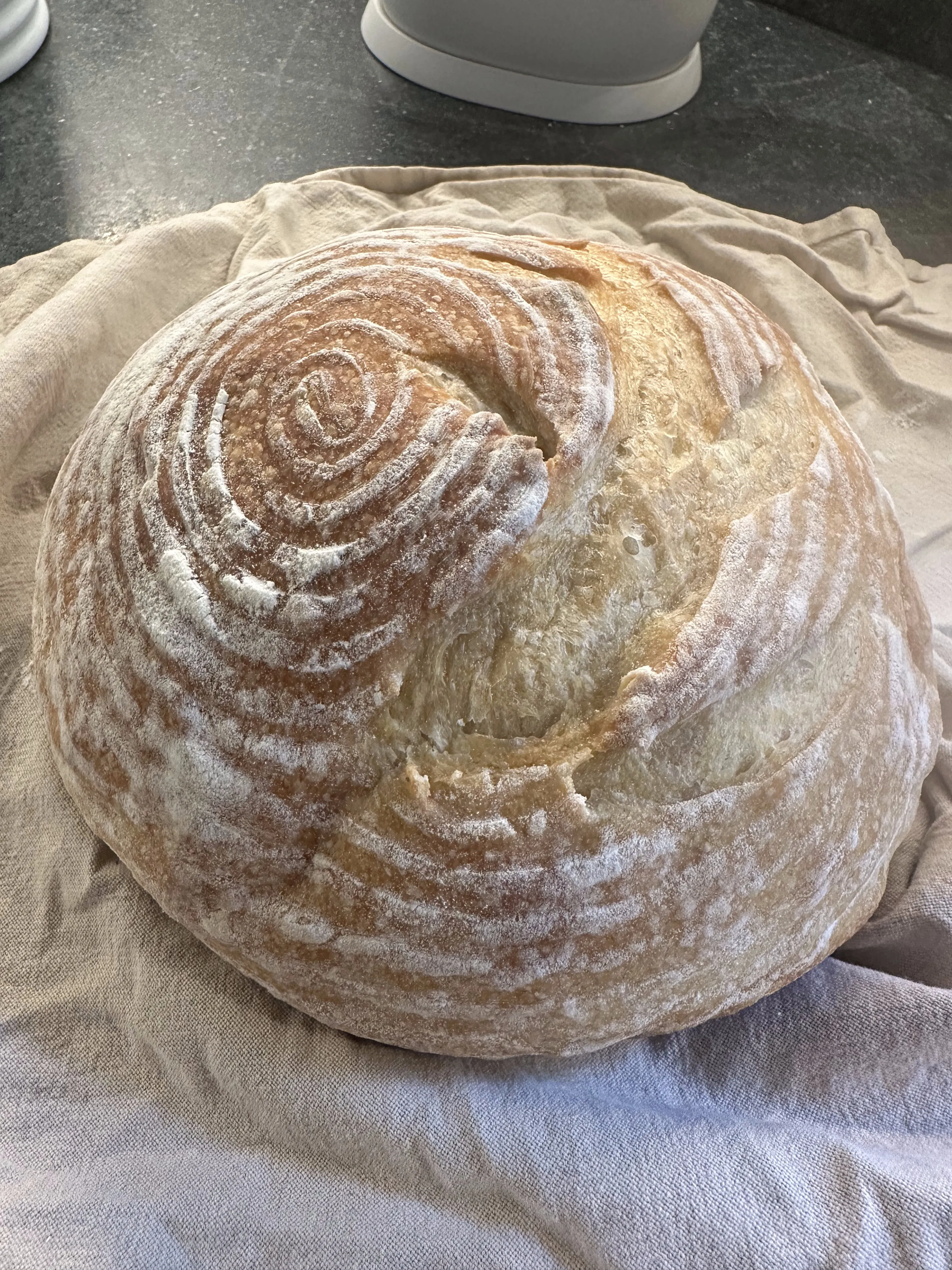 Round sourdough loaf with spiral score pattern on linen cloth